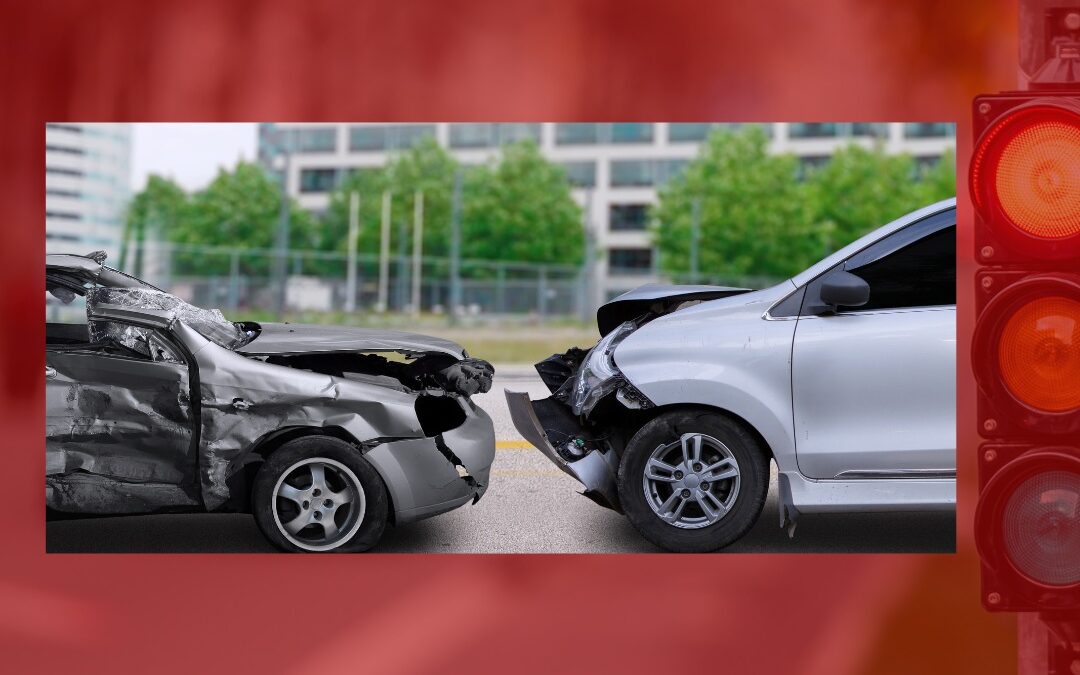 Two damaged cars, one with severe rear damage and the other with front damage, are stopped on a city street after a collision, framed by a red background and a traffic light