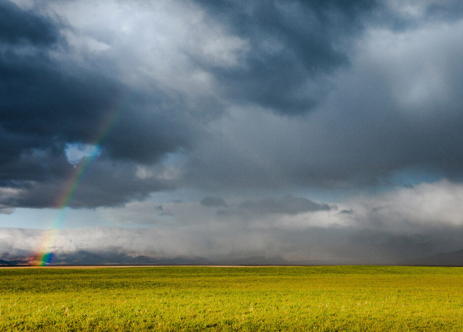 The dramatic scene features a rainbow emerging from dark, receding storm clouds